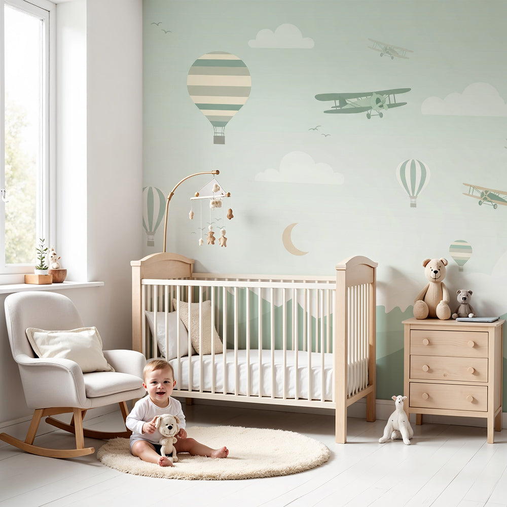 Kids-Mundo hot air balloon and biplane wall mural in a soft green nursery with a cot