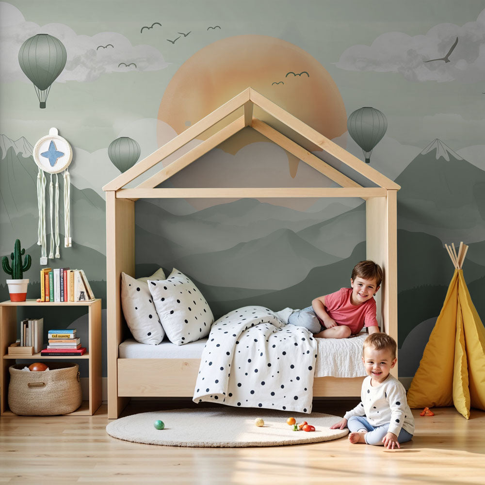 Kids-Mundo misty mountain and hot air balloon wall mural styled in a soft sage-green nursery with a cot