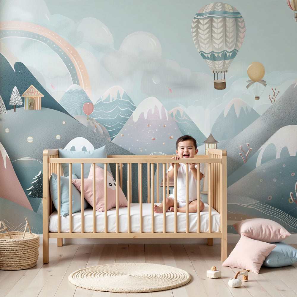 Kids-Mundo snowy village hot air balloon wall mural styled behind a cot in a soft pastel nursery