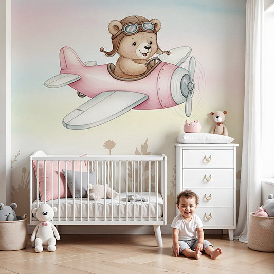 Kids-Mundo teddy bear pilot wall mural styled in a soft pastel nursery with a wooden cot.